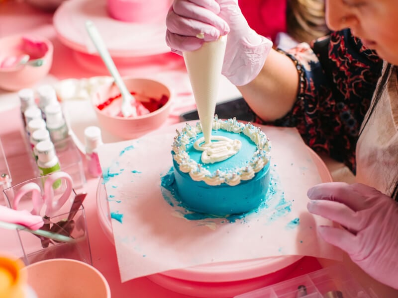 A close up of a person decorating a blue cake with white frosting